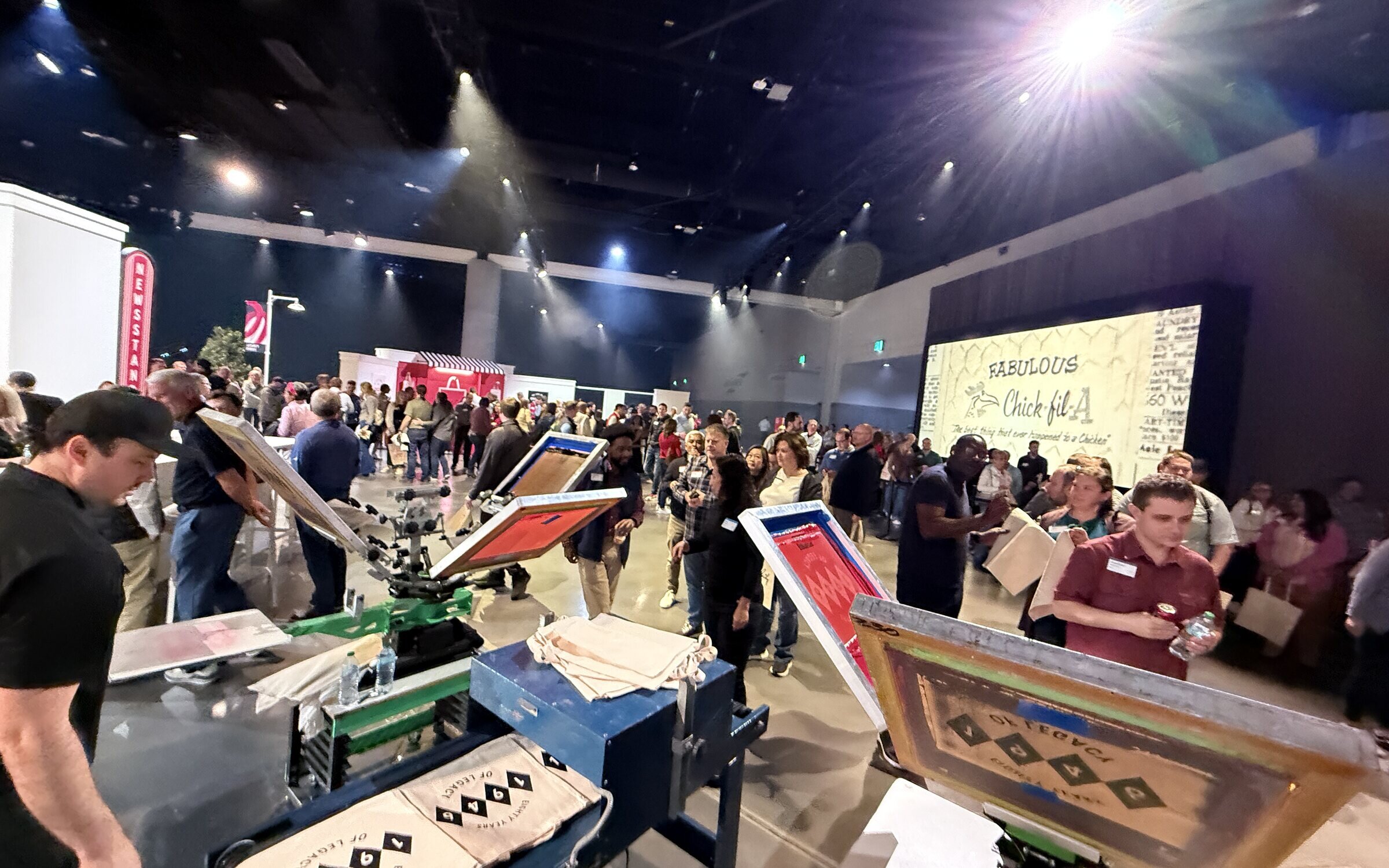 A packed corporate event hall with guests lined up around live screen-printing presses