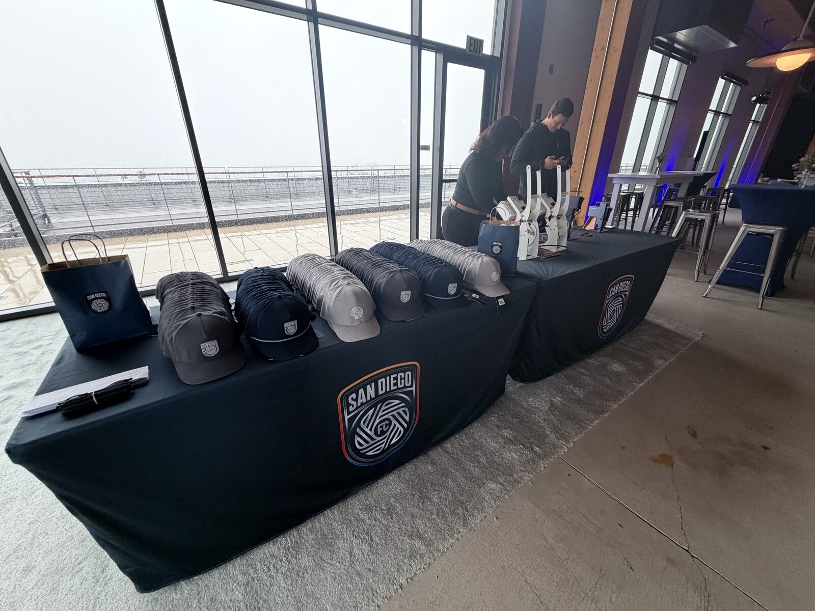 Embroidered caps arranged in rows on black merch tables at an upscale waterfront venue