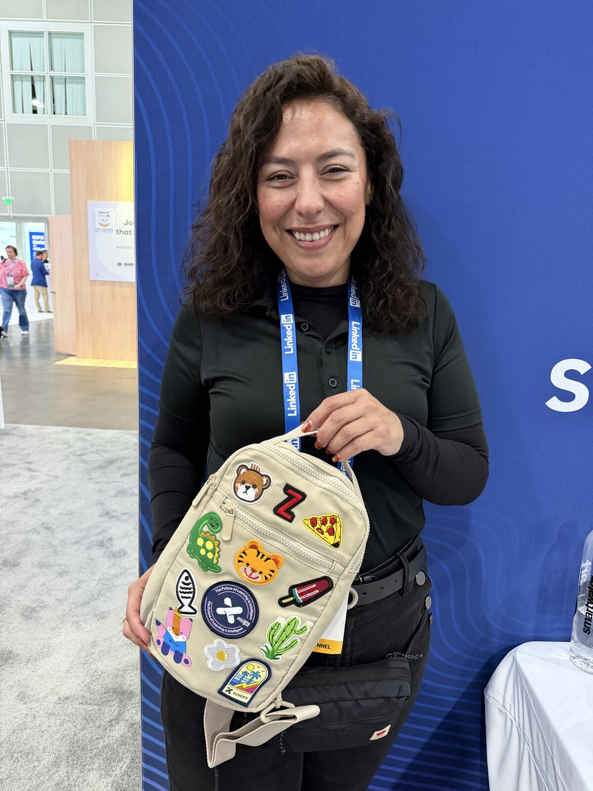 Crew member holding up a finished patch-covered sling bag at a convention booth