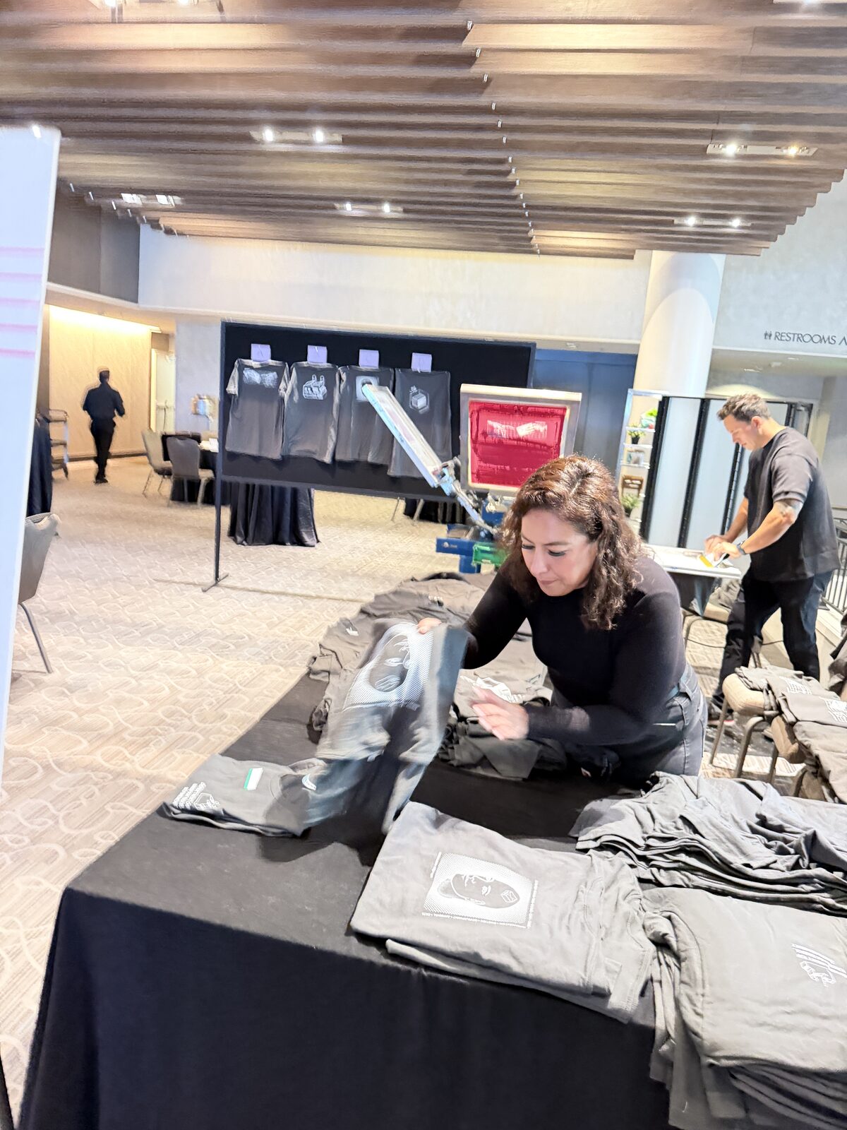 Crew member folding freshly printed shirts at a black-draped table at an elegant reception