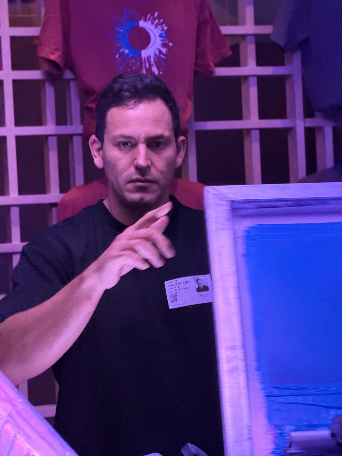 Screen printer adjusting a raised screen at a purple-lit evening reception with printed shirts behind