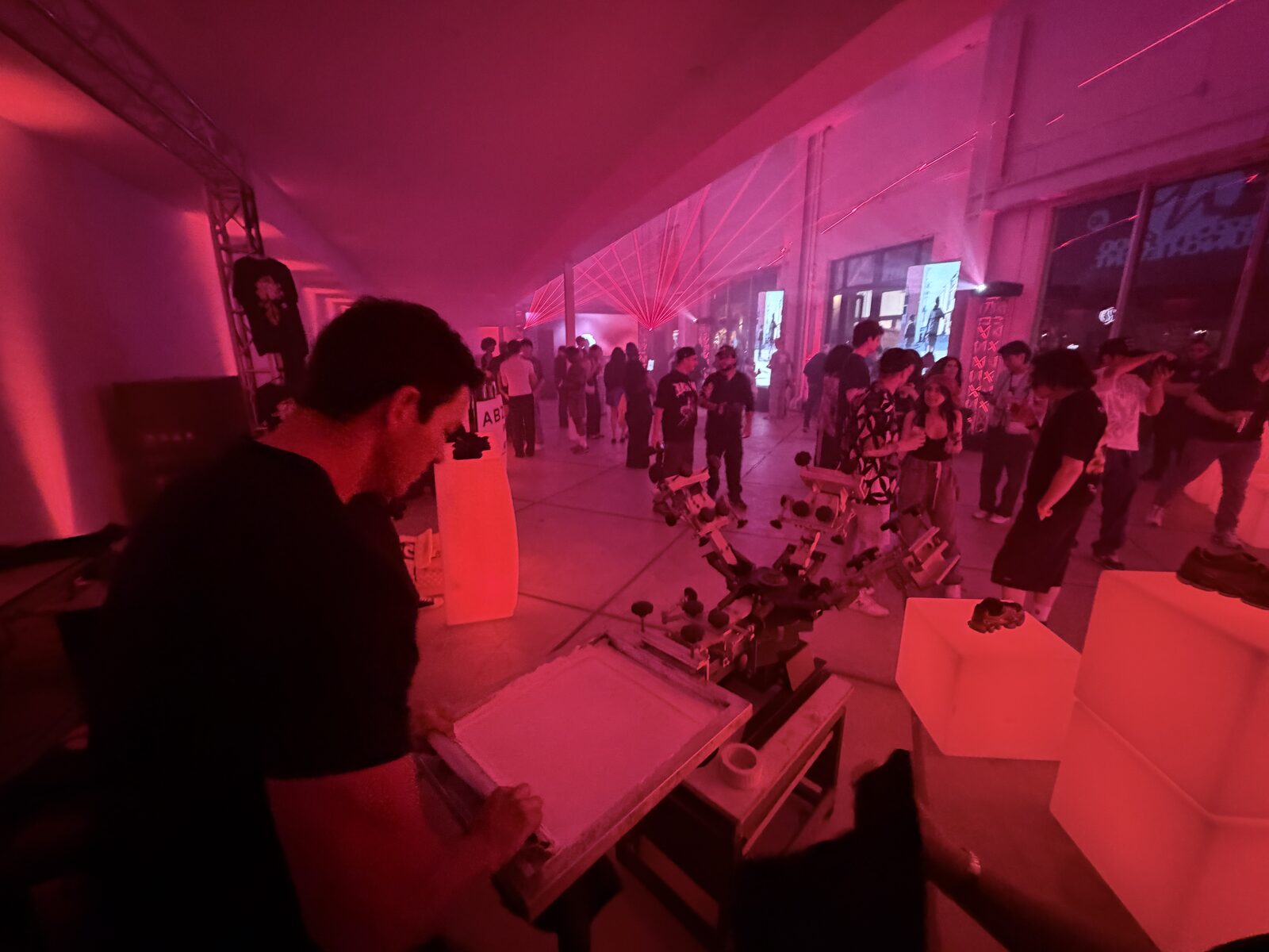 Printer flooding a screen at a four-color press while a crowd fills a red-lit night event