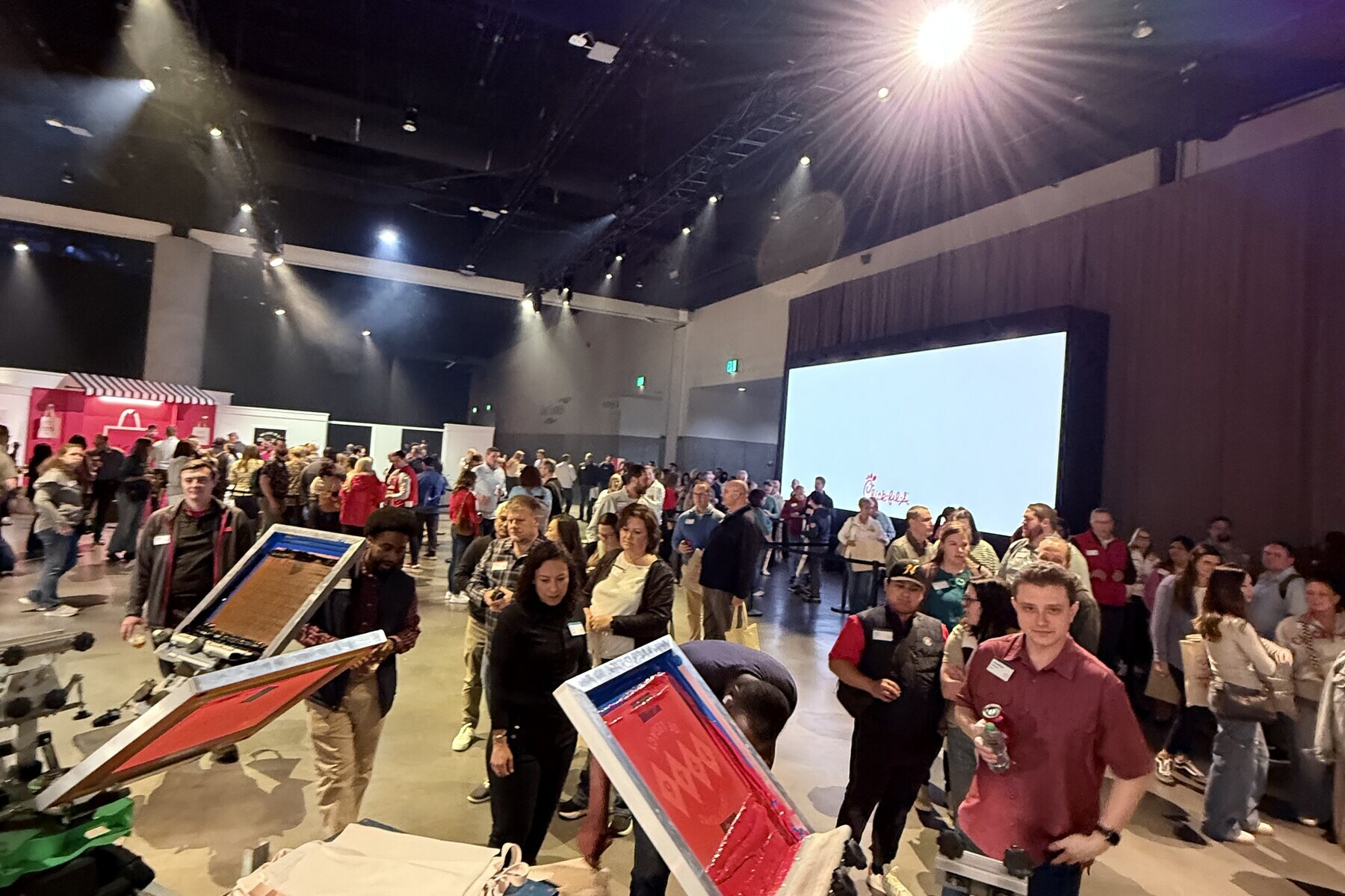 Crowd gathered around two screen-printing presses at a large indoor venue